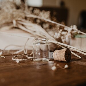 May include: A wooden USB drive shaped like a bottle with a cork top. The drive is sitting on a wooden table with dried flowers and twine.