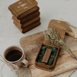 May include: A wooden box with a green moss lining and a wooden USB drive inside. The USB drive is engraved with the text "Day & Date".