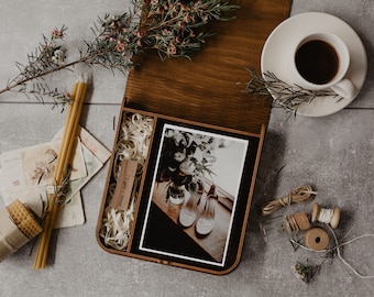 May include: A wooden box with a hinged lid, containing a photograph of a bouquet of white flowers and a pair of white shoes. The box also includes a small wooden USB drive with the text "Light & Stone" engraved on it. The box is surrounded by various items, including candles, a cup of coffee, and twine.