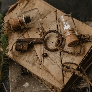 May include: Two glass vials with cork stoppers containing USB drives, an old rusty key, and a piece of twine on top of a stack of old, worn books.