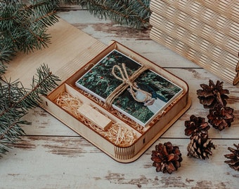 Könnte beinhalten: Eine Holzkiste mit einem Foto eines Paares in einer Waldlandschaft. Die Kiste ist mit Holzspänen und einem kleinen Holz-USB-Stick gefüllt. Die Kiste ist von Kiefernästen und Tannenzapfen umgeben.