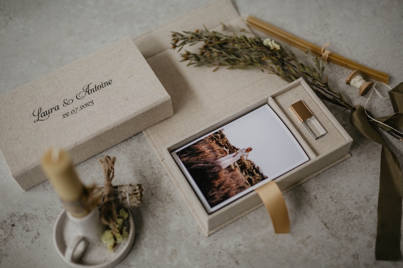 May include: A beige linen box with a photo print and a USB drive inside. The box is engraved with the text "Laura & Antoine 22.07.2023".