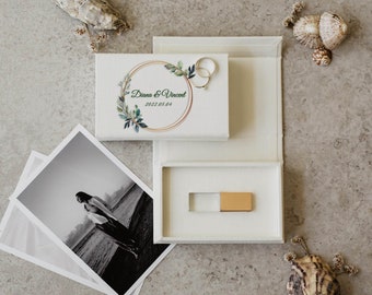 May include: A white wedding photo box with a gold USB drive, a black and white photo, and a gold ring. The box has the names "Diana & Vincent" and the date "2022.05.04" printed on it. The box is decorated with a floral design.