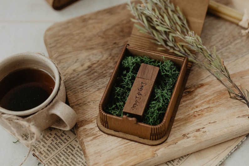 Peut inclure: Une cl&eacute; USB rectangulaire en bois brun fonc&eacute; avec le texte grav&eacute; Daisy & Daliah, nich&eacute;e dans une petite bo&icirc;te en bois assortie remplie de mousse verte. La cl&eacute; pr&eacute;sente une finition lisse et un capuchon, pr&eacute;sent&eacute;e dans un &eacute;tui de rangement.