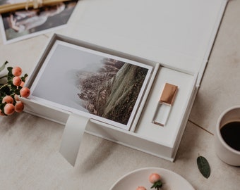 May include: A white box with a photo of a mountain range and a small, clear USB drive with a rose gold top. The box is open and the USB drive is sitting in a slot.