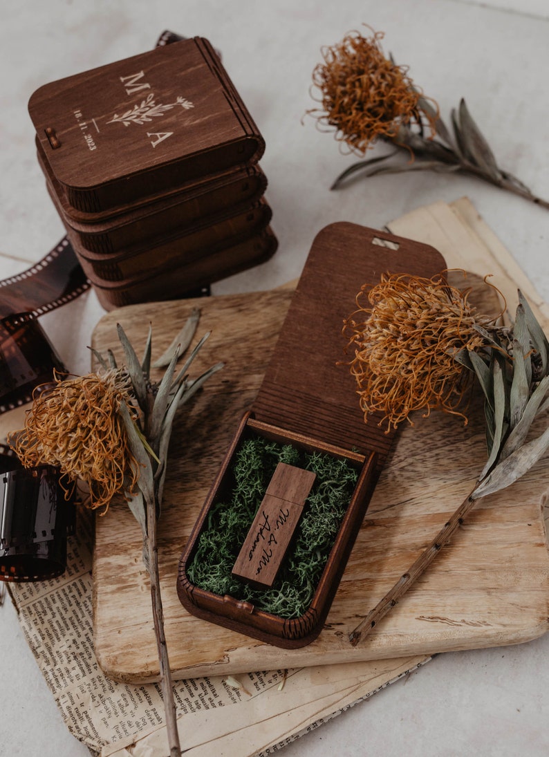 Peut inclure: Une cl&eacute; USB en bois brun fonc&eacute; grav&eacute;e avec le texte Mr. & Mrs. Adamo, nich&eacute;e dans une bo&icirc;te en bois assortie remplie de mousse verte. Le couvercle de la bo&icirc;te pr&eacute;sente les lettres grav&eacute;es M & A et la date 18. 11. 2023.