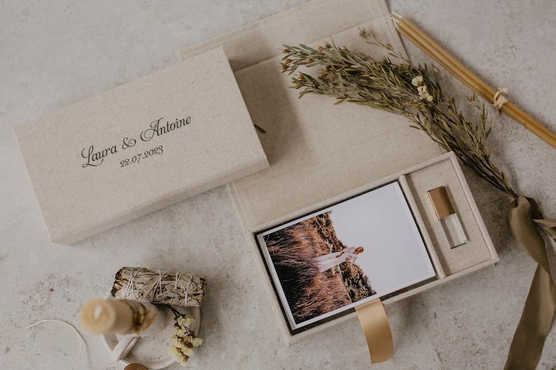 May include: A beige linen box with a photo print and a USB drive inside. The box is personalized with the text "Laura & Antoine 22.07.2023".