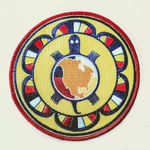 May include: Embroidered patch with a turtle design and a map of North America. The patch has a yellow background, a red border, and a blue turtle. The design includes red, white, and black accents. The patch is circular.