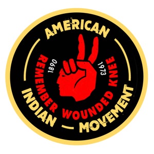 May include: A black and yellow circular sticker with the text "American Indian Movement" and "Remember Wounded Knee 1973 1890" around the edge. A red hand with two fingers raised in a peace sign is in the center of the sticker.
