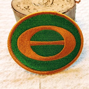Könnte beinhalten: Ein gestickter Aufnäher in Grün und Orange mit einem stilisierten Buchstaben "E" in der Mitte.