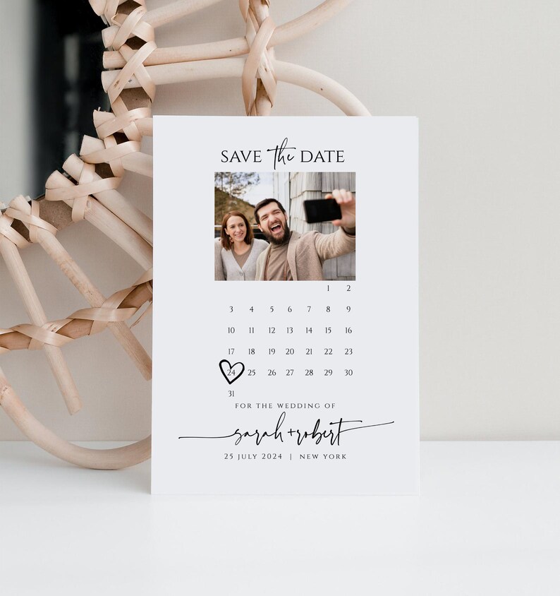 May include: Save the date card with a calendar featuring a heart on July 25th. The card has a photo of a couple taking a selfie and the text "SAVE The DATE" and "FOR THE WEDDING OF sarah+robert 25 JULY 2024 | NEW YORK".