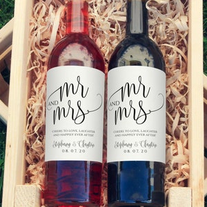 May include: Two wine bottles with white labels that say "Mr. and Mrs." in black cursive script. The labels also include the text "Cheers to love, laughter and happily ever after!" and the names "Stephany & Clayton" and the date "08.07.20".