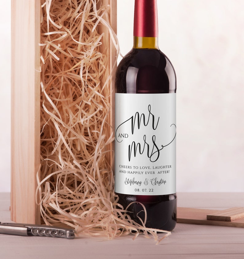 May include: A white wine bottle label with black calligraphy that reads "mr & mrs" and the text "Cheers to love, laughter and happily ever after!"  The label also includes the names "Stephany & Clayton" and the date "08. 07. 22".