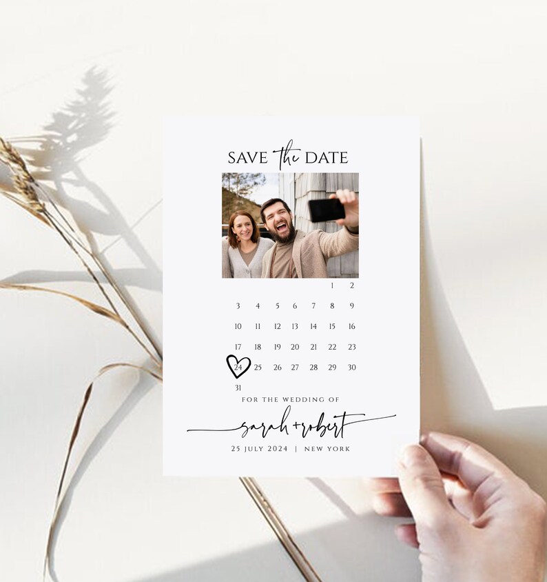 May include: Save the Date card with a calendar featuring a photo of a couple. The date 25 is circled with a heart. The text reads "Save the Date" and "For the wedding of Sarah + Robert" with the date "25 July 2024" and location "New York".