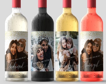 May include: Four wine bottles with red caps and custom labels. Each label features a photo of two women and the text "WILL YOU BE MY bridesmaid" or "flower girl". The bottles contain white, red, yellow, and pink wine.