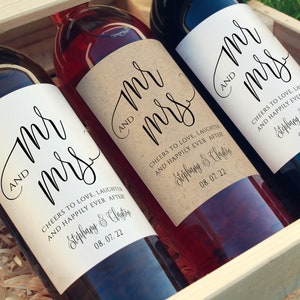 May include: Three wine bottles with personalized labels that say "Mr. and Mrs." with the couple's names and wedding date. The labels are printed on a kraft paper background.