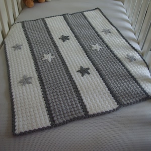 Op de afbeelding: Een grijs en wit gestreept babydekentje met een stervormig patroon. Het dekentje is gehaakt en heeft een zachte, textuur.