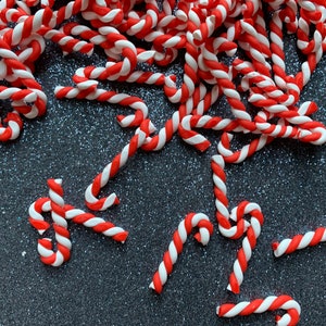May include: A pile of red and white candy canes on a sparkly silver background.