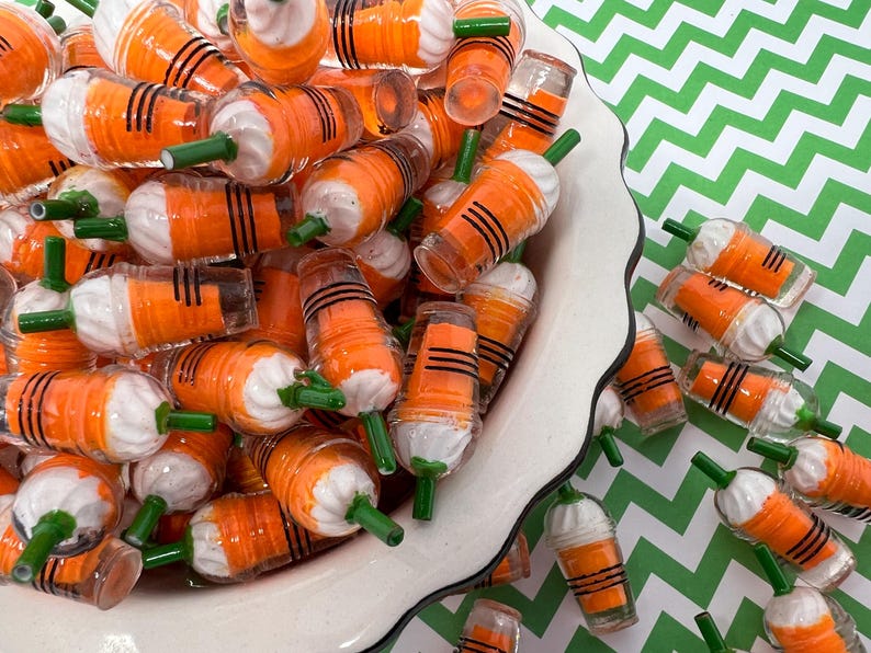 K&ouml;nnte beinhalten: Eine wei&szlig;e Sch&uuml;ssel gef&uuml;llt mit Miniatur-Bechern aus orangefarbenem und wei&szlig;em Kunststoff mit gr&uuml;nen Strohhalmen. Die Becher sind in einem zuf&auml;lligen Muster angeordnet und einige fallen aus der Sch&uuml;ssel auf eine gr&uuml;n-wei&szlig; karierte Oberfl&auml;che.