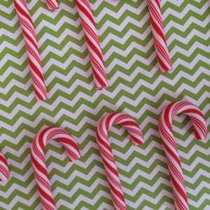 May include: A close-up of candy canes on a green and white chevron patterned background. The candy canes are red and white.