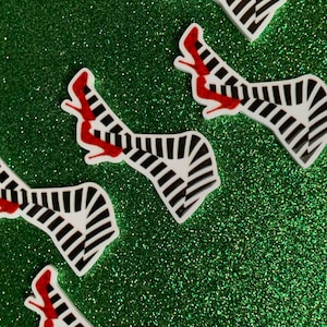 May include: Four white, black and red striped legs with red shoes. The legs are in a crossed position and are on a green glitter background.