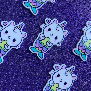 May include: Four white cat mermaid charms with a pink, purple, and blue tail holding a yellow star. The charms have a heart and a unicorn horn on their heads.
