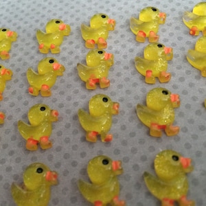 May include: A collection of yellow rubber duck figurines with orange feet. The ducks are arranged in rows on a gray surface.