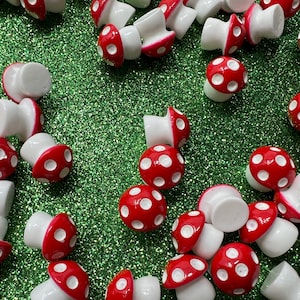 May include: A collection of red and white mushroom-shaped charms with white polka dots. The charms are made of plastic and have a glossy finish.