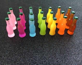 May include: A collection of miniature glass bottles in various colours, including pink, blue, green, yellow, and orange. The bottles have green tops and are arranged in a row on a dark grey surface.