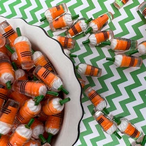 K&ouml;nnte beinhalten: Eine Sch&uuml;ssel gef&uuml;llt mit Miniatur-Karottenbechern in Orange und Wei&szlig; mit gr&uuml;nen Strohhalmen. Die Becher sind in einem zuf&auml;lligen Muster angeordnet und einige fallen aus der Sch&uuml;ssel.