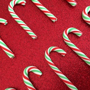 May include: Red and green candy canes on a red glitter background.