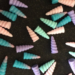 Peut inclure: Une collection de charmes de corne de licorne de couleur pastel dans des tons de rose, bleu et violet. Les cornes sont en plastique et ont un design en spirale.