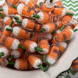 K&ouml;nnte beinhalten: Eine Sch&uuml;ssel gef&uuml;llt mit orangefarbenen und wei&szlig;en Karotten-Getr&auml;nkeanh&auml;ngern mit gr&uuml;nen Strohhalmen. Die Anh&auml;nger sind aus klarem Kunststoff mit schwarzen Streifen und wei&szlig;em Frosting oben.