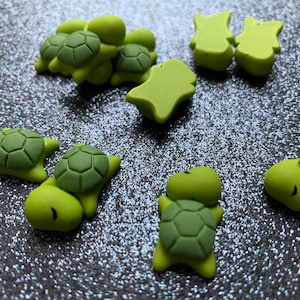 May include: A collection of green turtle-shaped charms, some with a shell pattern, and a few other green charms in various shapes.