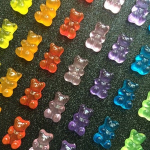 May include: Assortment of gummy bear shaped candies in various colors, including red, orange, yellow, green, blue, purple, and pink. The gummy bears are arranged in rows on a black background.