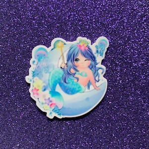 May include: A sticker featuring a cartoon mermaid with blue hair and a crown, sitting on a crescent moon with a starfish and flowers. The mermaid is holding a wand and has a winking expression.