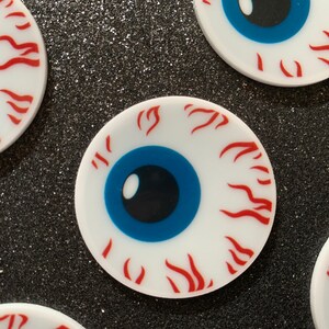 May include: Four white round stickers with a blue eye and red flames around the eye. The stickers are on a black background.