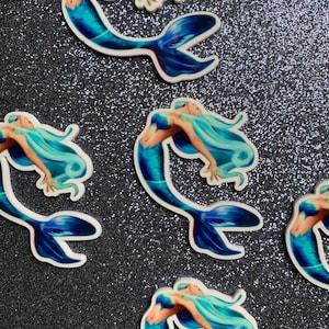 May include: Four mermaid stickers with blue tails and light blue hair. The mermaids are in a swimming pose with their tails curled up.