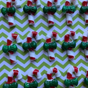 May include: A collection of red and white candy cane ornaments with green bows. The ornaments are arranged in rows on a green and white chevron patterned surface.