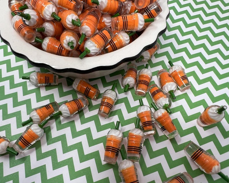 K&ouml;nnte beinhalten: Eine Sch&uuml;ssel gef&uuml;llt mit orangefarbenen und wei&szlig;en Miniatur-Plastikbechern mit gr&uuml;nen Strohhalmen. Die Becher sind auf einer gr&uuml;n-wei&szlig;en Chevron-Oberfl&auml;che verstreut.