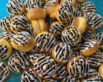 May include: A close-up of a pile of miniature cinnamon rolls with white icing and a swirl pattern. The rolls are arranged in a random pattern and are all the same size.