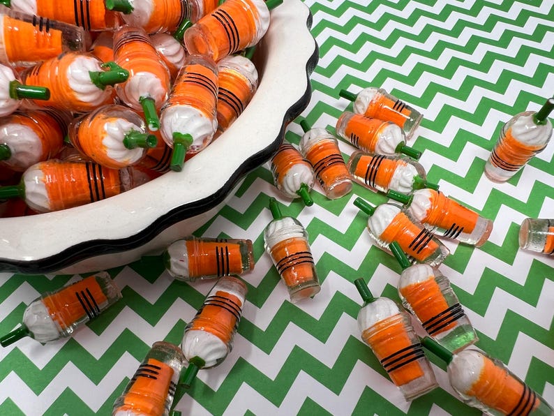 K&ouml;nnte beinhalten: Eine wei&szlig;e Sch&uuml;ssel gef&uuml;llt mit orangefarbenen und wei&szlig;en Miniatur-Plastikbechern mit gr&uuml;nen Strohhalmen. Die Becher sind auf einer gr&uuml;n-wei&szlig;en Chevron-Oberfl&auml;che verstreut.