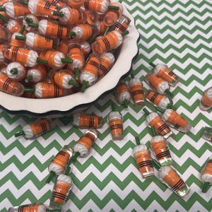 K&ouml;nnte beinhalten: Eine Sch&uuml;ssel gef&uuml;llt mit orangefarbenen und wei&szlig;en Miniatur-Plastikbechern mit gr&uuml;nen Oberteilen. Die Becher sind auf einer gr&uuml;n-wei&szlig;en Chevron-Oberfl&auml;che verstreut.