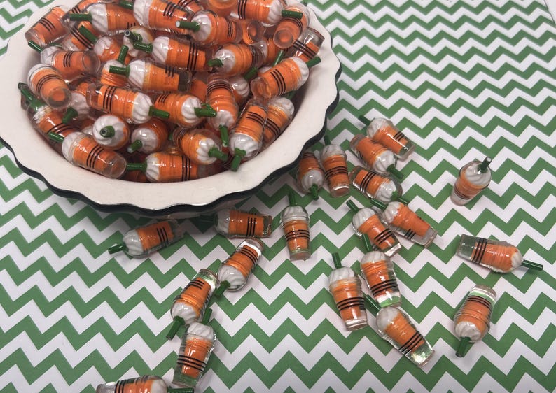 K&ouml;nnte beinhalten: Eine Sch&uuml;ssel gef&uuml;llt mit orangefarbenen und wei&szlig;en Miniatur-Plastikbechern mit gr&uuml;nen Oberteilen. Die Becher sind auf einer gr&uuml;n-wei&szlig;en Chevron-Oberfl&auml;che verstreut.