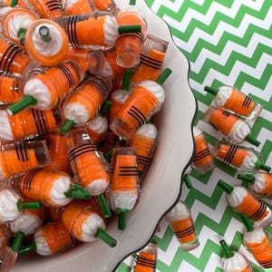 K&ouml;nnte beinhalten: Eine wei&szlig;e Sch&uuml;ssel gef&uuml;llt mit orangefarbenen und wei&szlig;en Miniatur-Plastikbechern mit gr&uuml;nen Strohhalmen. Die Becher haben schwarze Streifen und &auml;hneln Miniatur-Eiskaffee-Getr&auml;nken.