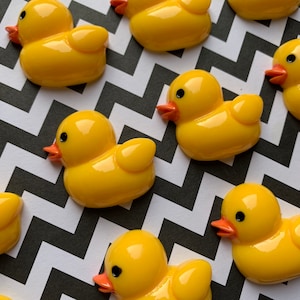 May include: A group of yellow rubber duck toys with orange beaks and black eyes. The ducks are arranged in a staggered pattern on a black and white chevron background.