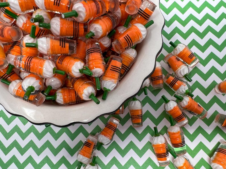 K&ouml;nnte beinhalten: Eine wei&szlig;e Sch&uuml;ssel gef&uuml;llt mit Miniatur-Plastikbechern in Orange und Wei&szlig; mit gr&uuml;nen Strohhalmen. Die Becher sind auf einer gr&uuml;n-wei&szlig;en Chevron-Oberfl&auml;che verstreut.