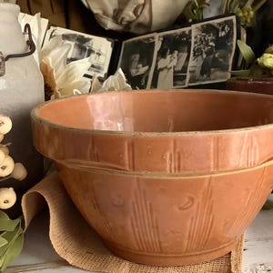 May include: A tan ceramic mixing bowl with a wide rim and a textured exterior featuring vertical lines and small circular indentations. The bowl has a smooth, glazed finish and a deep, rounded basin, showcasing a consistent warm, earthy color throughout.
