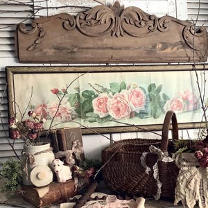 May include: A collection of home decor items including a rectangular framed print of pink roses, a dark brown woven basket, a ceramic jar with a lid, a small white figurine, old books, dried flowers, and a piece of cream-colored lace fabric.