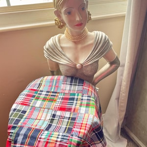 May include: A decorative statue of a woman with blonde hair, wearing a pearl necklace and a silver-colored dress. The statue is positioned in front of a colorful plaid fabric, featuring red, blue, green, and white squares.